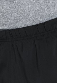 Černý elastický pas se sbíranými detaily v kombinaci se šedým upnutým topem, který se vyznačuje hladkou texturou a měkkým materiálem.