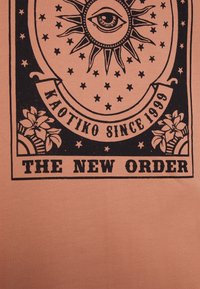 T-shirt pesca con un design grafico nero che presenta un occhio, raggi di sole, stelle e piante tropicali, con il testo: "KAOTIKO SINCE 1999" e "THE NEW ORDER."
