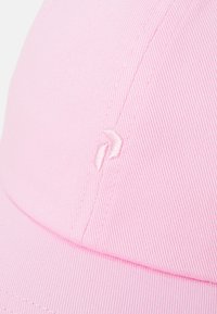 Casquette rose en tissu texturé. Elle présente un logo brodé sur le côté, avec un design subtil. La visière est légèrement courbée.