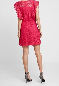 Spetsekjol i livlig rosa med korta fladdrande ärmar, scallopkant och en figurnära silhuett, matchad med svarta glittriga högklackade skor.