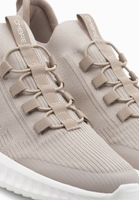 Scarpe sportive beige con tomaia in maglia texturizzata, sistema di allacciatura elastica e suola in gomma solida con un accento bianco.