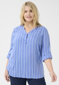 Blau gestreifte Bluse mit hochgeschlagenen Ärmeln, Knopfdetail und V-Ausschnitt. Hergestellt aus einem leichten Stoff mit vertikalen gelben Streifen.