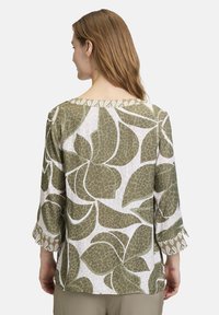 Groene en witte blouse met een patroon en driekwart mouwen, met een bladerenontwerp en een ronde halslijn, gemaakt van lichte stof.