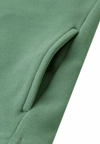 Tessuto felpato verde con una texture morbida. Presenta un'apertura per tasca cucita e cuciture pulite lungo i bordi.