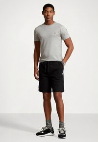 Pilkas trumpomis rankovėmis marškinėlis su mažu logotipu, derinamas su juodais šortais su raišteliu ir pilkomis kojinaitėmis su raštais, baigtas juodais sportiniais batais.