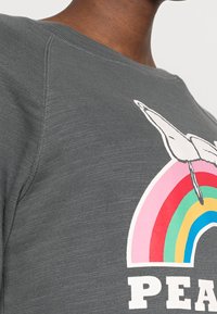 Sudadera gris con un gráfico colorido de un arcoíris, un unicornio blanco y la palabra "PAZ" en letras blancas y en negrita. Textura suave.