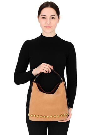 Tan suede handtas met een gebogen silhouet, voorzien van gouden studs langs de onderkant en een bruin leren handvat.