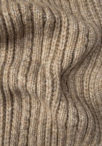 Tissu tricoté beige avec un motif texturé en côtes. La laine douce et épaisse crée une apparence confortable. Les coutures visibles et les plis superposés ajoutent de la profondeur.