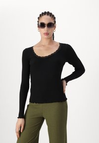Top negru cu dungi, cu mânecă lungă și dantelă pe decolteu, cu un tiv cu margini ondulate, asortat cu pantaloni verzi măslinii cu dungi.
