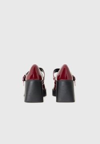 Red patent leather shoes with a black chunky heel, featuring an adjustable ankle strap and a smooth surface texture.