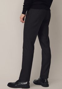 Czarne spodnie o dopasowanym kroju, wykonane z tkaniny o fakturze, z dwoma bocznymi kieszeniami oraz gładkim, prostym krojem nogawek. Zestawione z czarnymi eleganckimi butami.