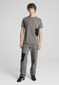 Szary strój sportowy z okrągłym dekoltem, zawierający T-shirt z czarną kieszenią i zamkiem, w zestawie z dopasowanymi spodniami z czarnymi akcentami i kieszeniami.