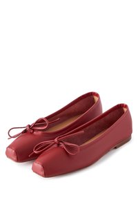 Paar rode leren ballerina's met vierkante neuzen en decoratieve strikjes, weergegeven op een witte achtergrond.