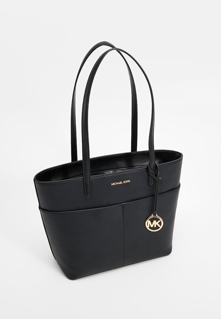 Zwarte leren tote bag met twee lange handvatten, voorzien van een gouden logo charm en een verhoogde merknaam aan de voorkant. Gladde textuur, rechthoekige vorm.