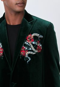 Green velvet jacket featuring intricate floral and snake embroidery in red, black, and blue, with a single button closure and peaked lapels.