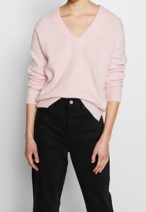 Light pink v-neck sweater made of soft knit material. Features ribbed cuffs and hem, styled with black high-waisted jeans.