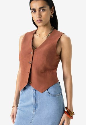 Brown linen vest with a V-neckline, featuring five buttons and a tailored fit. Paired with a light blue denim skirt.