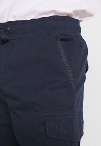Shorts cargo bleu marine en tissu léger, dotés d'une ceinture élastique, de poches latérales et d'un ourlet retroussé avec un logo embossé.