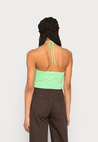 Top halter em verde menta com textura canelada e laços ajustáveis no pescoço, combinado com calças castanhas de cintura alta, apresentando um design casual.