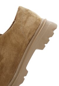 Zapato de ante marrón con una suela ligeramente elevada y una suela de goma texturizada que presenta un patrón de zigzag para mayor tracción.