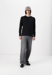 Black long-sleeve shirt, grey baggy jeans, and black sneakers. Wearing a light grey cap with a logo on the front. Simple, casual attire.