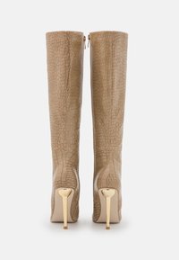 Bottes hautes jusqu'au genou, beige, avec un motif texturé effet crocodile. Elles présentent un talon stiletto doré et une fermeture éclair latérale.