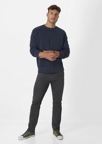 Marineblaues Sweatshirt mit Rundhalsausschnitt und gerippten Bündchen, kombiniert mit dunkelgrauen Slim-Fit-Jeans und grünen Leinenschuhen mit weißen Sohlen.