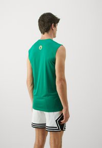 Green sleeveless shirt made of soft fabric, featuring a round neckline and a logo on the upper back. Worn with white mesh shorts.
