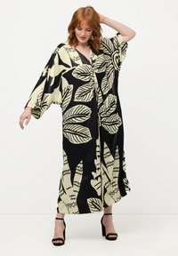 Černý a krémový kaftan s lístkovým vzorem, volný střih, výstřih do V, široké rukávy a délka ke kotníkům, doplněný černými sandály na podpatku.