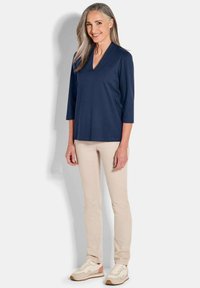 Marineblauw V-hals shirt met driekwartmouwen, gecombineerd met beige slim-fit broeken en lichte sneakers met roze accenten. Glad stoftextuur.