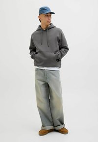 Szara bluza z kapturem i sznurkiem, jasnoniebieska czapka, jasne, luźne dżinsy i brązowe buty na slip-on. Prosty design, casualowy krój, brak widocznych wzorów.