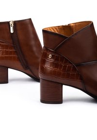 Bottes cheville en cuir marron présentant un motif crocodile texturé sur le talon, une fermeture éclair sur le côté et un talon en bois rond.