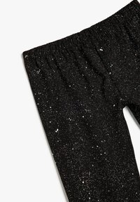 Czarne legginsy z elastycznym pasem, z rozproszonym wzorem brokatowym przypominającym gwiazdy na tkaninie. Miękka tekstura.