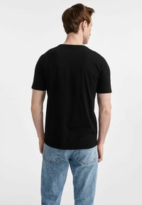 Czarny bawełniany t-shirt z krótkim rękawem i okrągłym dekoltem, zestawiony z jasnoniebieskimi dżinsami, widok z tyłu.