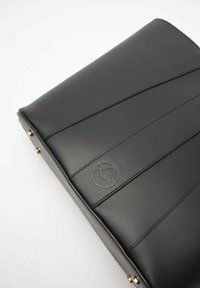 Czarna skórzana torba z przeszytymi panelami, wytłoczonym logo i metalowymi akcentami. Gładka tekstura, prostokątny kształt.