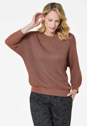 Brauner gerippter Pullover mit lockerer Passform, weiten Ärmeln und rundem Ausschnitt, kombiniert mit schwarzen gemusterten Hosen. Weiche Textur sichtbar.