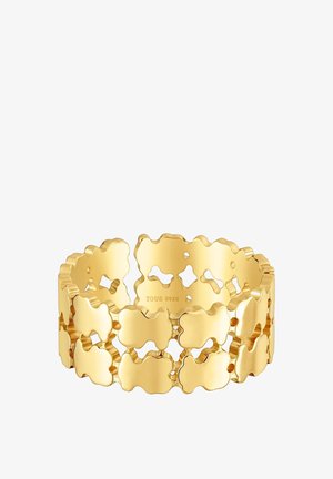 Gold-tone bracelet with a cut-out design featuring wavy shapes, smooth texture, and a polished finish. Engraved 'TOUS S925' inside.