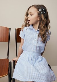 Robe à carreaux bleu clair avec des manches courtes, fermeture à boutons sur le devant et dentelle en bordure. Présente une jupe évasée et un tissu doux et lisse. Pinces à cheveux incluses.