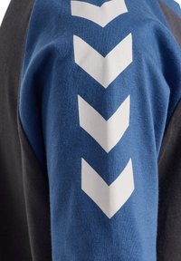 Svart och blå långärmad skjorta med texturerat tyg. Blå sektion har tre stora vita chevronmönster på axeln.