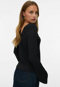 Czarny top z długim rękawem, wykonany z teksturowanej tkaniny, z delikatnym dekoltem w kształcie litery V i rozkloszowanymi rękawami. W połączeniu z ciemnoniebieskimi dżinsami.
