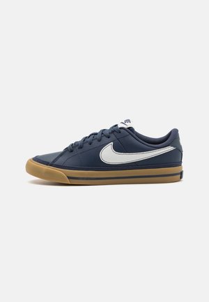 Baskets Nike bleu marine avec swoosh blanc, semelle en gomme, design bas et fermeture à lacets sur un fond gris clair uni.