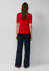 Czerwona bluzka z krótkim rękawem połączona z ciemnymi, szerokimi spodniami. Materiał wydaje się być miękki; spodnie mają podwinięte nogawki z gładkim wykończeniem.