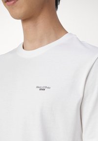 Witte katoenen t-shirt met een ronde hals en een klein zwart logo "Marc O'Polo DENIM" gedrukt aan de linkerkant van de borst.