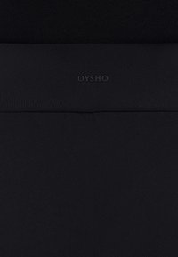 Schwarze Leggings aus dehnbarem Material, mit einer glatten Textur, breitem Bund und dezentem OYSHO-Logo am Bund.