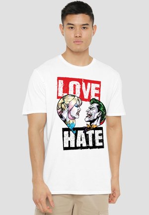 Man wearing white t-shirt with graphic of two faces shouting at each other inside a heart, with "LOVE" above and "HATE" below.