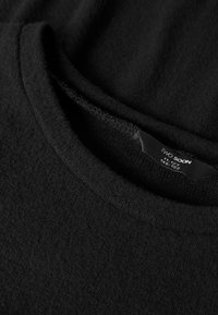 Mustast, pehmest kangast kampsun ümarate kaelustega. Nähtav silt kannab teksti "TWO SOON" ja märgib suurusvahemikku 11–14 aastat. Kampsunil on tekstuursete detailidega mustrikujundus.