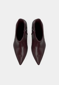 Pár tmavo burgundských členkových topánok s ostrou špičkou a bočnými zipsami, zobrazených zhora na jednoduchej bielej pozadí.