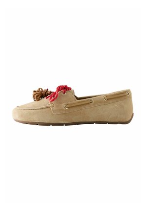 Beige suède loafer met rode veter en bruine leren kwast op witte achtergrond, zijaanzicht.