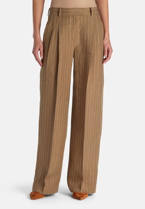 Plačios rudos kelnės su baltomis vertikaliomis siaurų dryželių juostomis, priekine klostė, diržo kilpos, dėvimos su smailiais rudais batais ir smėlio spalvos viršumi.