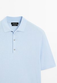 Světle modré polo tričko vyrobené z bavlny s texturovaným povrchem, s klasickým límečkem, krátkými rukávy a zapínáním na tři knoflíky.